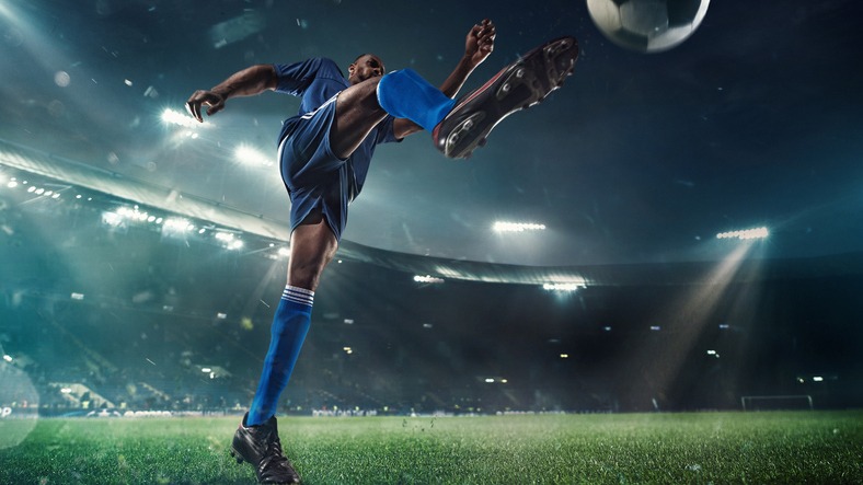 Football or soccer player in action on stadium with flashlights, kicking ball for winning goal, wide angle. Action, competition in motion